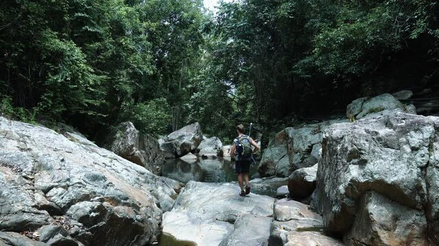 A tourist walks along a stone riverbed against the background of a backwater in the jungle