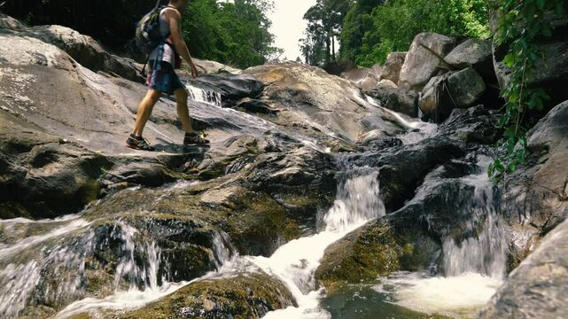 A tourist walks along a small cascading waterfall with branching streams in the middle of the jungle