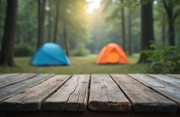 Selbstklebende Fototapeten Rustic wooden table with blurred camping scene, forest background. Blue, orange tents for travel, adventure. Summer landscape, vacation in wilderness. Wooden surface for product display, camping © Maryna