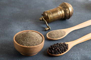 A bowl of black peppercorns on a gray background and a metal grinder
