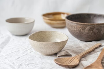 Colorful ceramic bowls of different sizes rest on a textured surface with wooden utensils