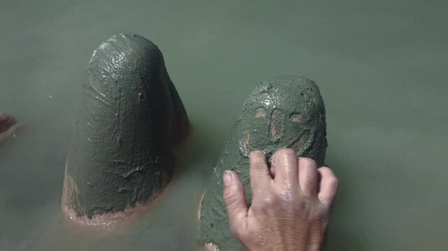 Man in a thermal wild lake applying volcanic healing mud to his body. Rupite, Bulgaria