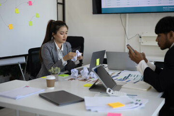 A group of people are sitting around a table with a laptop, a calculator, and a stack of papers. They are discussing business matters and looking at graphs and charts
