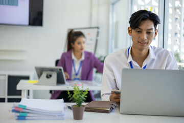 A group of people are sitting around a table with a laptop, a calculator, and a stack of papers. They are discussing business matters and looking at graphs and charts
