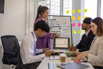 Obraz premium A group of people are sitting around a table with a laptop, a calculator, and a stack of papers. They are discussing business matters and looking at graphs and charts 