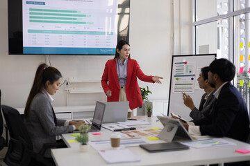 A group of people are sitting around a table with a laptop, a calculator, and a stack of papers. They are discussing business matters and looking at graphs and charts
