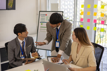 Three people in suits are sitting at a table with a laptop and a book. They are discussing something important
