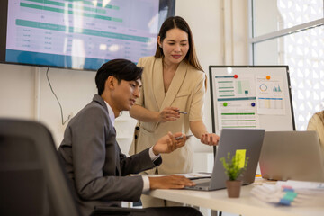 Two people in suits are looking at a presentation on a computer screen. One of them is pointing at the screen
