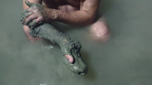 Man in a thermal wild lake applying volcanic healing mud to his body. Rupite, Bulgaria