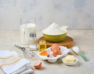 Step-by-step preparation of thin pancakes or crepes on a light background. Prepared ingredients for cooking crepes.