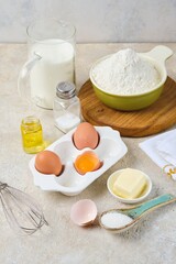 Step-by-step preparation of thin pancakes or crepes on a light background. Prepared ingredients for cooking crepes.