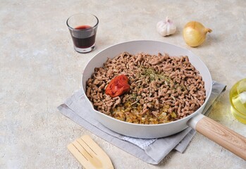 Step-by-step preparation of pancake lasagna or casserole with pancakes and minced meat on a light concrete background. Preparation of minced meat filling in a light frying pan.