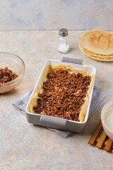 Step-by-step preparation of pancake lasagna or casserole with pancakes and minced meat on a light concrete background.