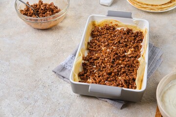 Step-by-step preparation of pancake lasagna or casserole with pancakes and minced meat on a light concrete background.
