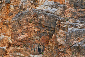 Close-up view of a rocky cliff with diverse shades of brown, orange, and gray, showcasing detailed textures, stratifications, and geological formations.
