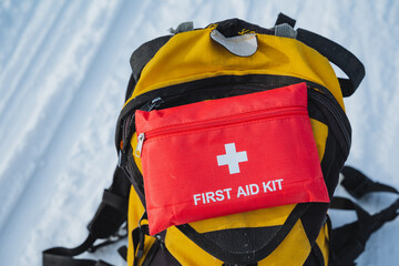A bright yellow backpack featuring a prominently placed red first aid kit attached to it, making it easily visible and prepared for any emergency situations that might arise