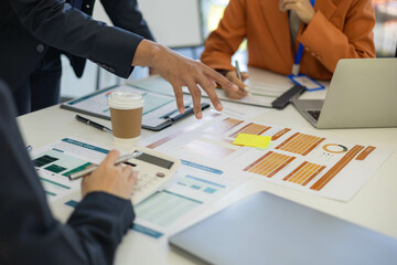 A woman in an orange shirt is looking at a piece of paper with graphs on it. She is holding a cup of coffee in front of her. The scene suggests that she is working on a project or analyzing data
