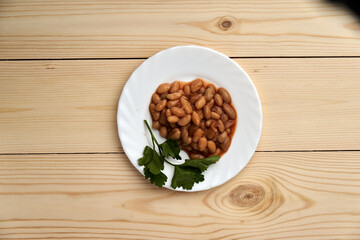 A plate of beans and parsley sits on a wooden table. The beans are spread out and appear to be cooked. The parsley is placed on the edge of the plate, adding a pop of color and freshness to the dish