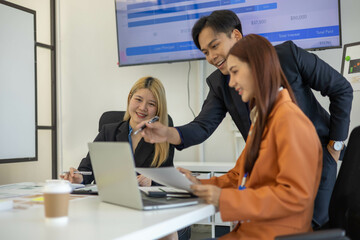 Three people are sitting at a table with a laptop open. One of them is laughing while the other two...