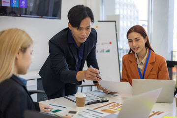 Three people are sitting at a table with a laptop open. One of them is laughing while the other two look on. The man in the middle is giving a presentation to the other two

