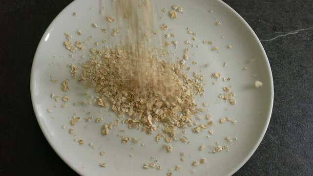 Oatmeal is trickling dowm onta a white plate, where it accumulates. Some also lands on the black table. 