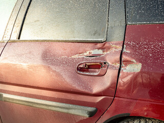 Red car door dented after accident, car hit. Impact damage. Damaged rear door of car, dent after...