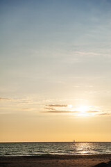 Obraz premium Golden sunset over the calm ocean with a sailboat on the horizon