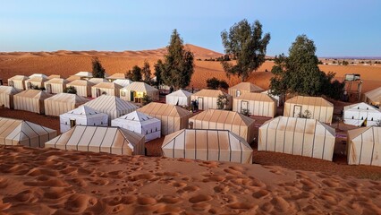 Desert camp with traditional tents in the sand dunes of Merzouga, Morocco, under a clear blue sky