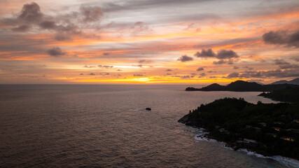 Dark silhouettes of islands stand against a warm sky at twilight, reflecting on the water. Seychelles, Mahe.