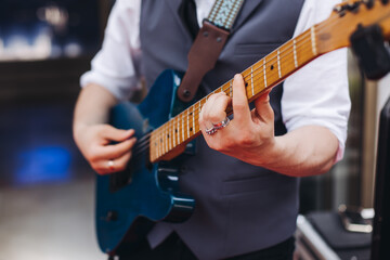 Fototapeta premium Concert view of an electric guitar player with vocalist and rock band performing in a club, male musician guitarist on stage with audience in a crowded concert show club hall arena, hands on a guitar