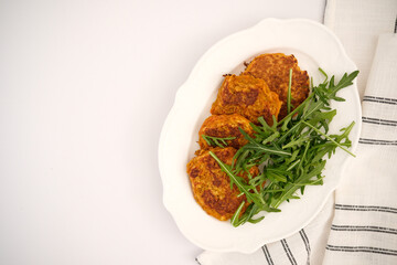 Carrot pancakes with rucola on white plate with napkin.