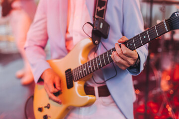 Obraz premium Concert view of an electric guitar player with vocalist and rock band performing in a club, male musician guitarist on stage with audience in a crowded concert show club hall arena, hands on a guitar