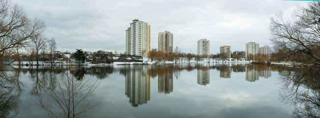 Fototapeta premium A modern residential area by a water body in the city, showcasing new home construction and the demolition of older structures. The urban landscape reflects the transition of winter into spring.