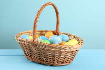 Many decorated Easter eggs in wicker basket on light blue wooden table