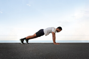 Determined male athlete performing plank exercise by the sea