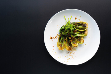 Dish features grilled bok choy garnished with spices on a minimalist black background.