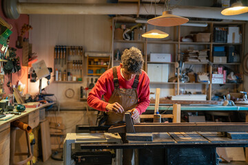 Man in woodworking shop use spatula to spread glue evenly before attaching leather pads to wood for future furniture. Table base assembly, precise craftsmanship, detail attention in handmade furniture