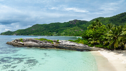 Rocky shoreline surrounded by turquoise waters and a dense tropical forest. Seychelles, Mahe. Anse...