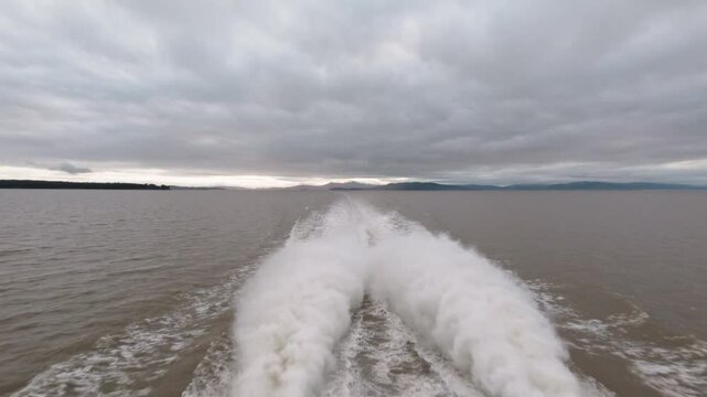 Footage of a wake behind a speed boat riding under a gray cloudy sky