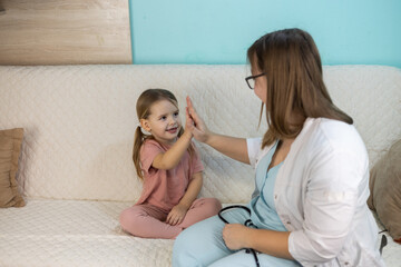 The doctor examined the child at home in a friendly and playful manner. The pediatrician gives a high five to a little girl sitting on the couch after a successful medical examination at home.
