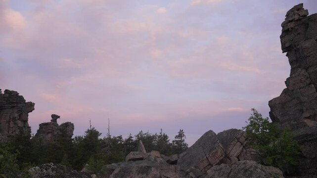 Stone pillars and balancing rocks stand tall against a backdrop of shifting pastel hues as the sun sets over the ural mountains, creating a dramatic and awe-inspiring natural spectacle
