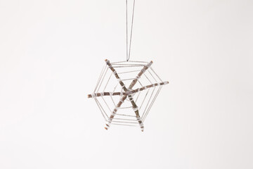 a handmade craft resembling a spider web. It is created using six small sticks arranged hexagonally, with white string wrapped around them to form the web. The craft hangs by a thin black string