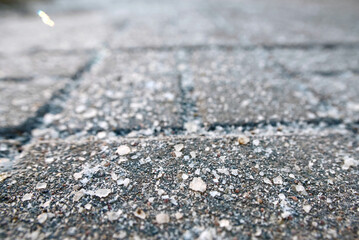 Sidewalk covered with de-icing salt during winter, harmful effects of uncontrolled use on health, environment, and urban surfaces. Selective focus.