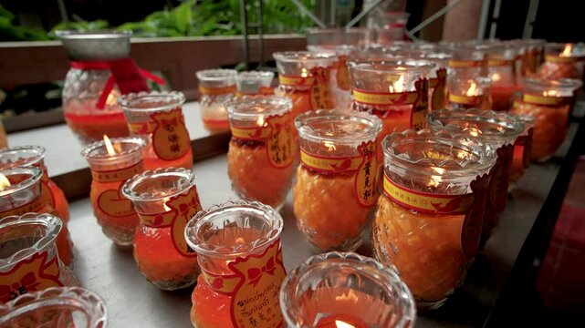 Orange candles burning inside glass jars, illuminating traditional chinese temple interior with soft, meditative glow