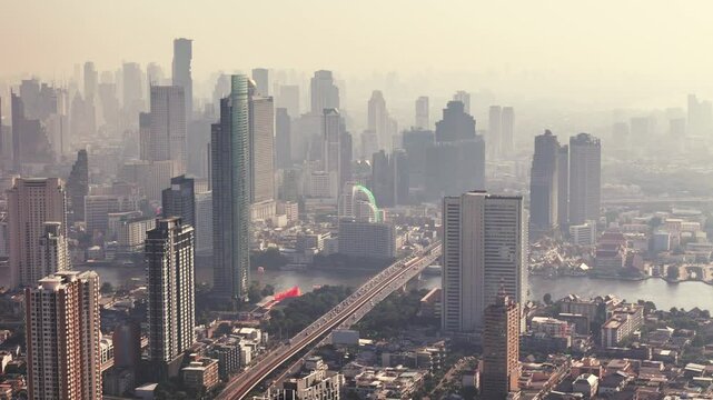 Bangkok towering skyscrapers of city reflect morning sunlight in mist smog. Silhouettes of tall buildings along Krung Thon Buri Road 60fps 