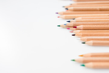Colorful wooden colored pencils arranged horizontally on white background