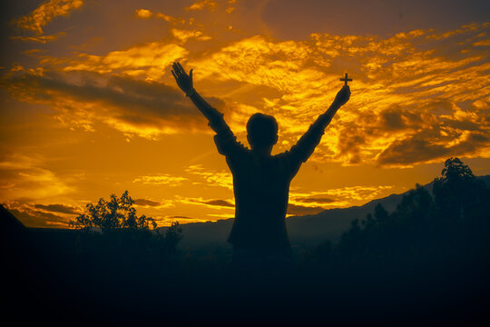 man standing praying and holding christian cross for worshipping God at sunset background. christian silhouette concept.