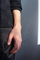 Vertical photo of a man's hand hanging freely along his body, part of a man's body in a blue...