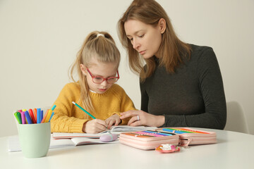Parental assistance. Mother helping her little daughter to prepare homework at home. Home education, homeschooling concept. 