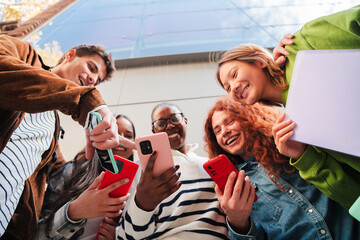 Obraz premium Group of cheerful friends enthusiastically sharing their smartphones and engaging in lively conversation while enjoying their time together in a bustling atmosphere of excitement and connection
